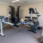 Fitness room with gym equipment, including a rowing machine, treadmill, cycling machine, and weights.