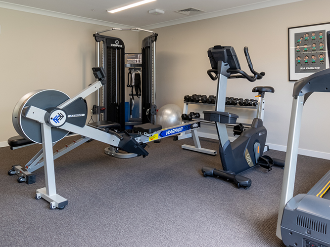 Fitness room with gym equipment, including a rowing machine, treadmill, cycling machine, and weights.