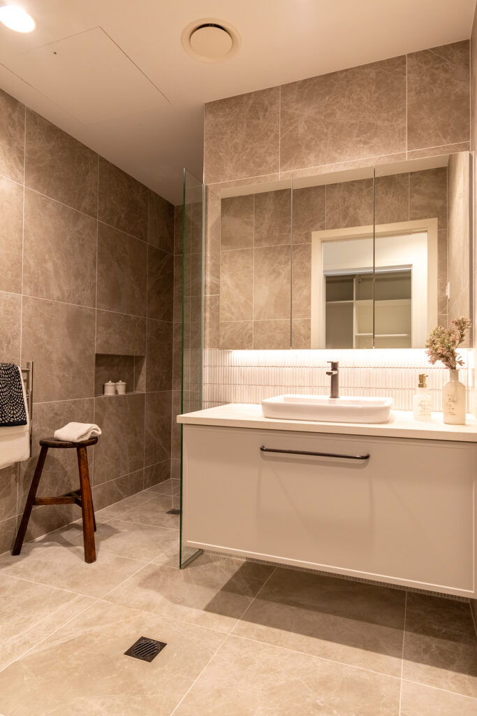 Modern bathroom at Rawhiti Estate retirement village with elegant tiles, glass shower, and a vanity unit with a large mirror.