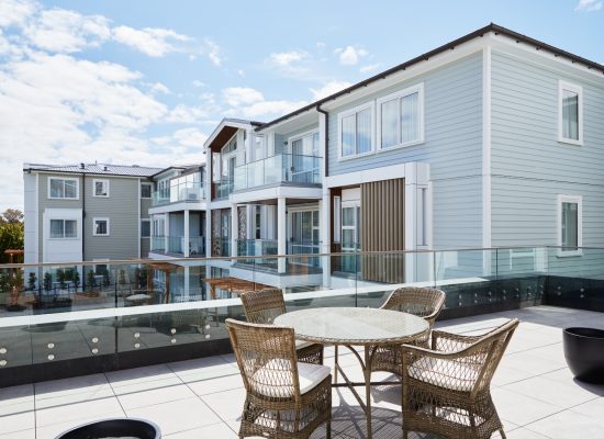 Outdoor seating area at Rawhiti Estate retirement village with wicker furniture and glass balcony railings.